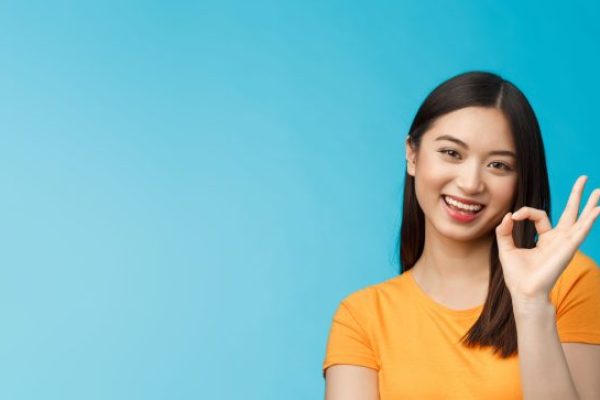 Close-up cute asian friendly girl supports your fantastic idea, smiling broadly, show okay ok sign approval, accept terms, agree take part event, stand blue background satisfied, judging nice work.
